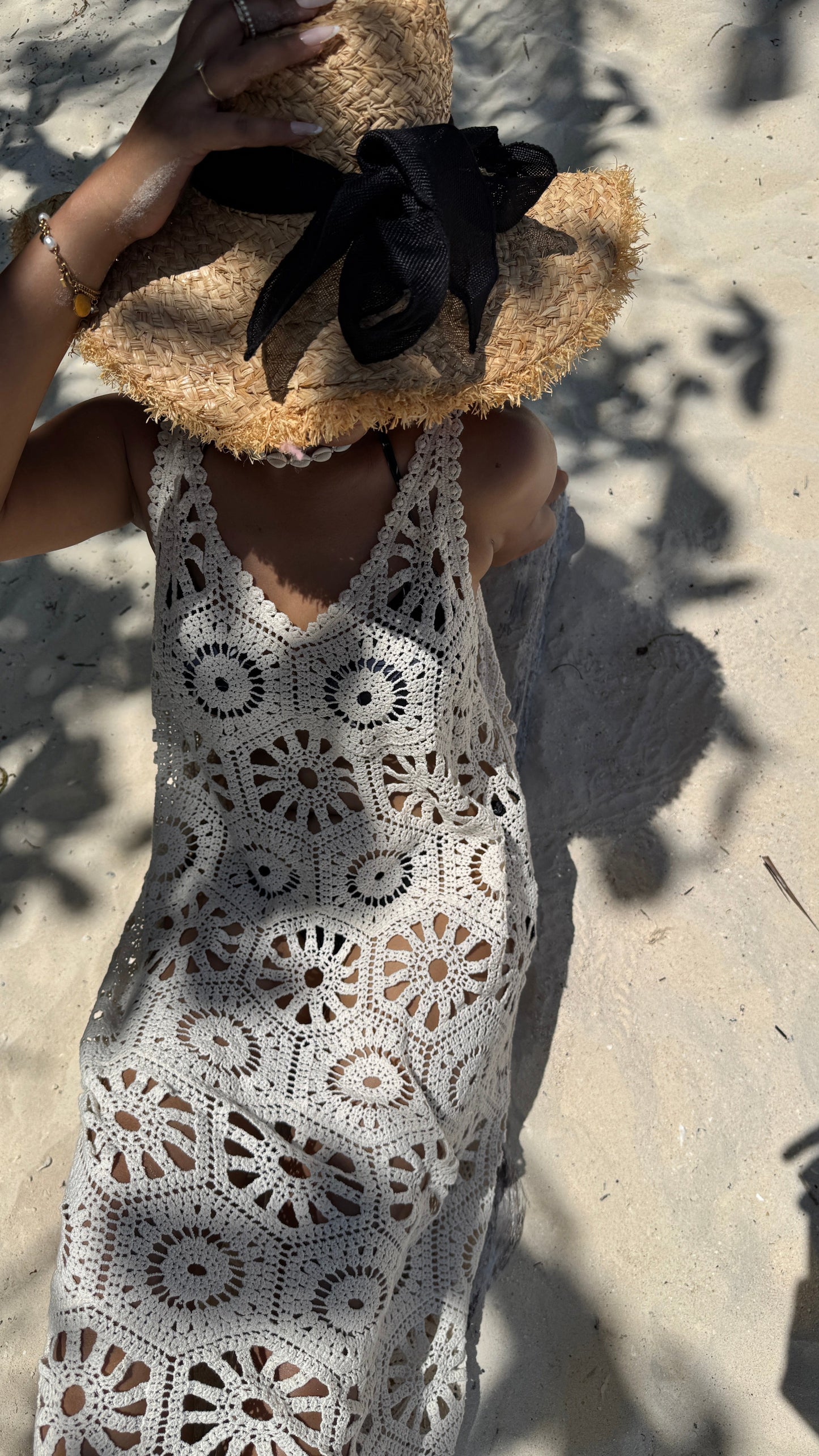 Person wearing a white crochet dress and straw hat on a sandy background