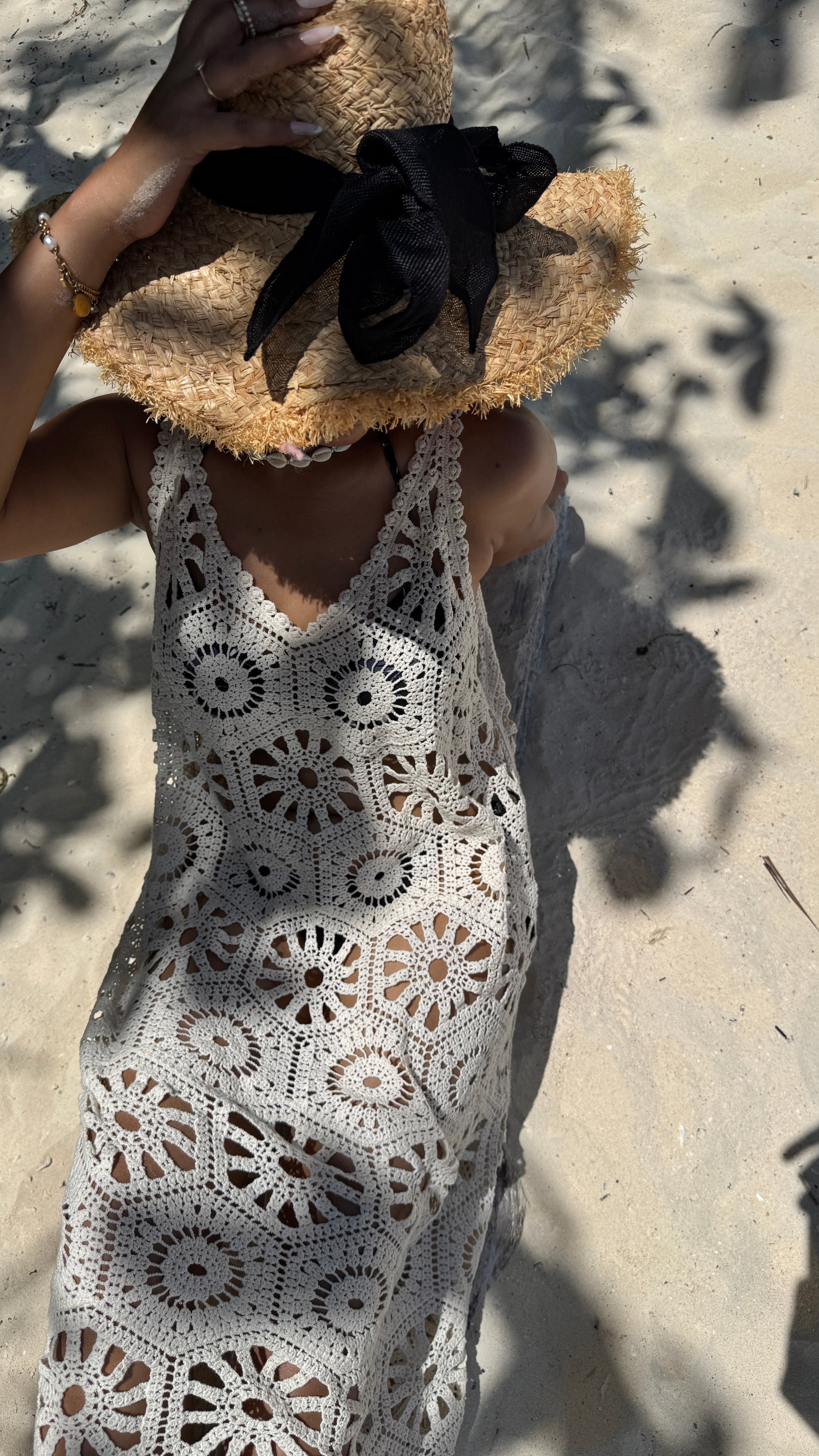 Person wearing a white crochet dress and straw hat on a sandy background